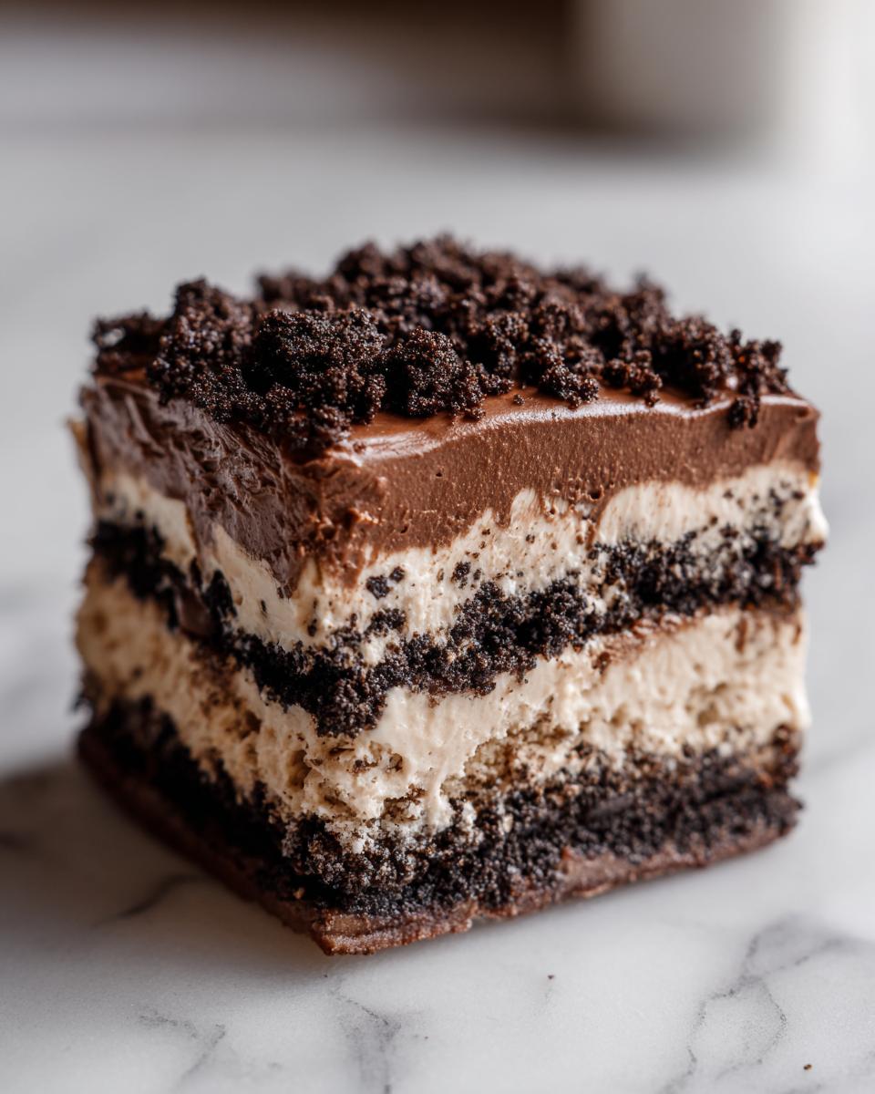 Close-up of a square slice of layered no-bake dirt cake featuring chocolate pudding, cream filling, and cookie crumbs.