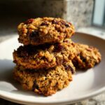 A stack of three golden brown oatmeal breakfast cookie loaded with dried cranberries on a white plate.
