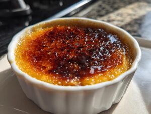 Close-up of a single serving of Creme Brulee in a white ramekin with a deeply caramelized, crackly sugar crust.