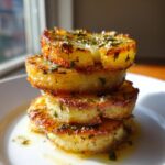 Three golden-brown potato stacks drizzled with garlic herb butter and sprinkled with herbs.