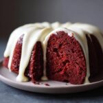 Close-up of a rich, deep red velvet bundt cake with a thick white glaze dripping down the sides.