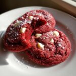 Close-up of two soft red velvet cake mix cookies dusted with powdered sugar and white chocolate chips.