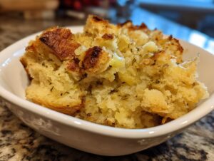 Close-up of a serving of moist and fluffy crock pot stuffing with visible herbs and celery in a white bowl.