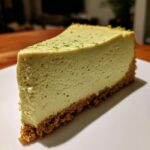 A close-up slice of creamy, pale green key lime cheesecake on a white plate, topped with lime zest.