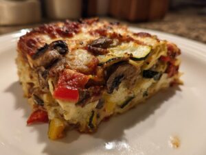 A close-up of a thick slice of roasted vegetable lasagna showing layers of zucchini, mushrooms, peppers, and cheese.