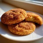 Three soft, thick Snickerdoodle cookies generously coated in cinnamon sugar, resting on a white plate.
