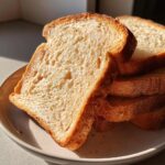 Close-up of stacked, soft slices of golden sourdough sandwich bread on a plate.