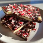 Close-up of stacked pieces of rich peppermint bark featuring dark chocolate, white chocolate, and crushed candy canes.