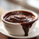 Close-up of rich, dark chocolate fondue steaming in a white bowl, dripping down the side.