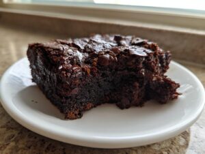 A close-up of a rich, dark slice of sweet potato brownies topped with melted chocolate chips on a white plate.