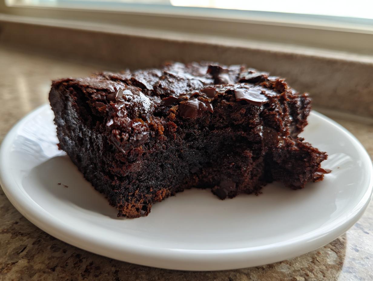 A close-up of a rich, dark slice of sweet potato brownies topped with melted chocolate chips on a white plate.