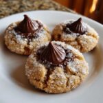 Close-up of three sugar-coated peanut butter blossoms cookies topped with chocolate kisses.