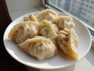 A close-up of several freshly steamed Traditional Chinese Dumplings arranged on a white plate near a window.