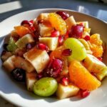 Close-up of a vibrant winter fruit salad featuring diced pears, orange segments, green and red grapes, and pomegranate seeds.