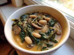 Close-up of a creamy white bean mushroom stew featuring cannellini beans, dark spinach, and sliced mushrooms.