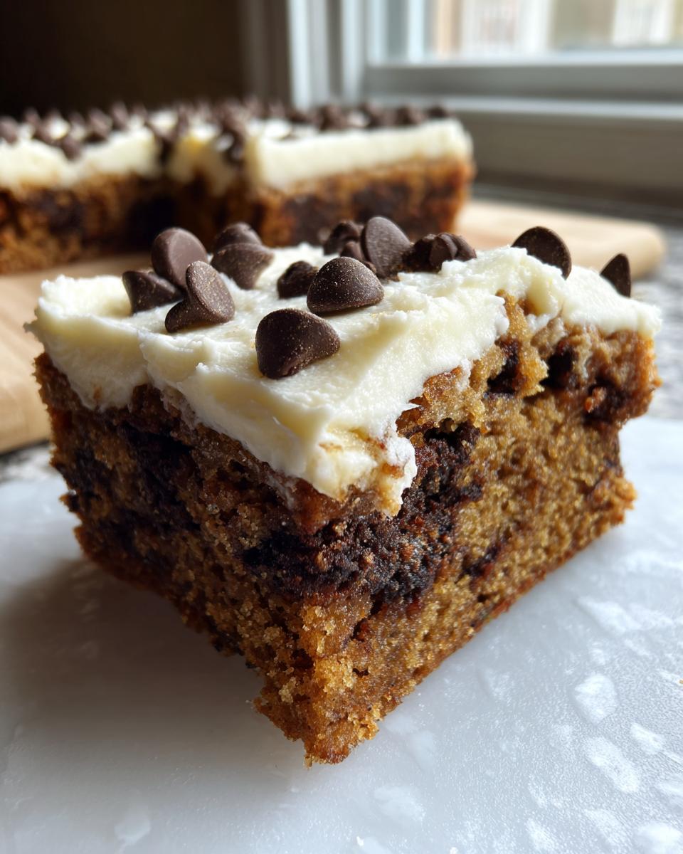 Close-up of a thick slice of amazing cookie cake recipe topped with white frosting and chocolate chips.