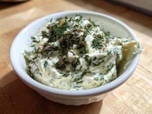 Close-up of creamy, homemade dill dip generously topped with fresh dill, served in a small white bowl.