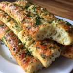 A stack of golden, soft garlic breadsticks topped with melted butter, cheese, and fresh parsley, showing the airy interior.