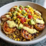 A close-up of a delicious shrimp bowl featuring grilled shrimp over quinoa, topped with corn salsa, avocado, and a creamy yellow sauce.