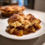 A close-up shot of a warm slice of apple cobbler showing caramelized apples and a thick, sugary crumb topping.