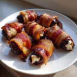 Six crispy, bacon-wrapped stuffed dates filled with cream cheese, served on a white plate.