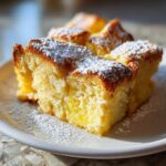 Close-up of squares of moist baked french toast dusted generously with powdered sugar on a white plate.