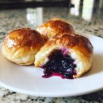 Close-up of a golden-brown Blueberry Pie Bomb cut open, showing rich, oozing blueberry filling.