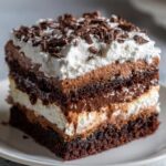 Close-up of a decadent slice of brownie refrigerator cake showing rich layers of chocolate cake, mousse, and whipped cream.