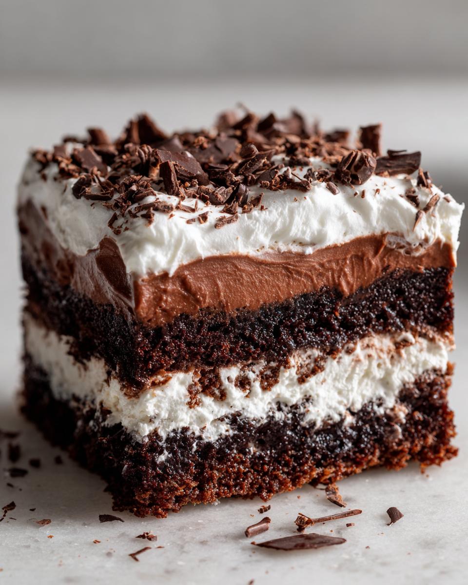Close-up of a rich slice of brownie refrigerator cake showing three distinct layers: dark chocolate cake, white cream, and chocolate mousse, topped with whipped cream and chocolate shavings.