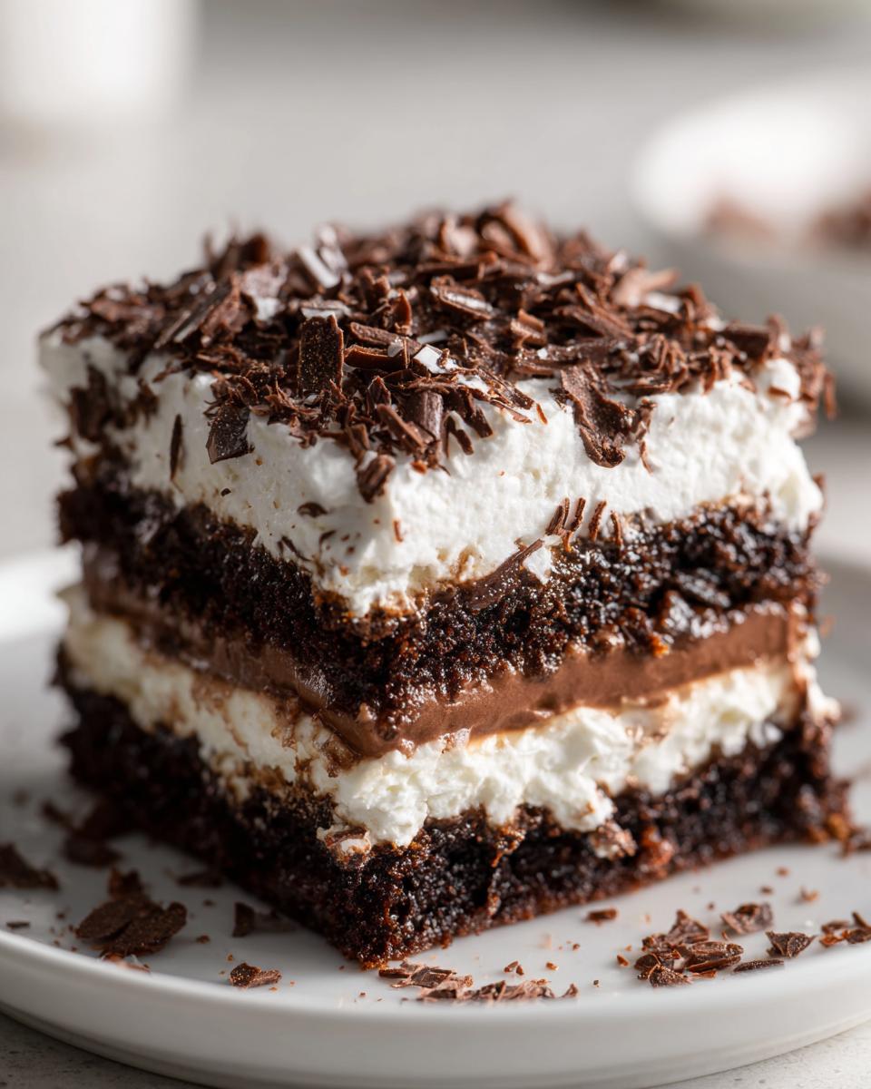 Close-up of a rich slice of brownie refrigerator cake showing three distinct layers of dark chocolate cake, cream, and pudding, topped with chocolate shavings.