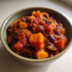 Close-up of a rustic bowl filled with thick, rich butternut squash chili and black beans.