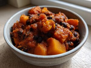 Close-up of a rustic bowl filled with rich, orange butternut squash chili and black beans.