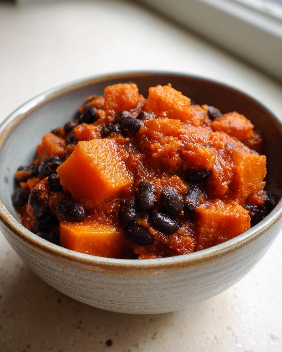 A close-up view of a hearty bowl of butternut squash chili featuring large orange chunks and black beans in a rich sauce.
