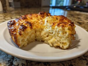 A close-up of a cheesy, golden-brown slice of baked mashed potatoes casserole on a white plate.