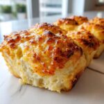 Close-up of baked hawaiian roll garlic bread with a bubbly, golden-brown, cheesy topping.