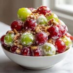 A white bowl filled with creamy chicken salad chick grape salad, topped with red and green grapes and chopped pecans.