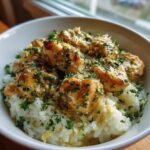 A bowl filled with creamy garlic parmesan rice topped with saucy chicken scampi pieces and fresh parsley.