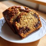 Two thick slices of moist banana bread recipe with melted chocolate chips on a white plate.