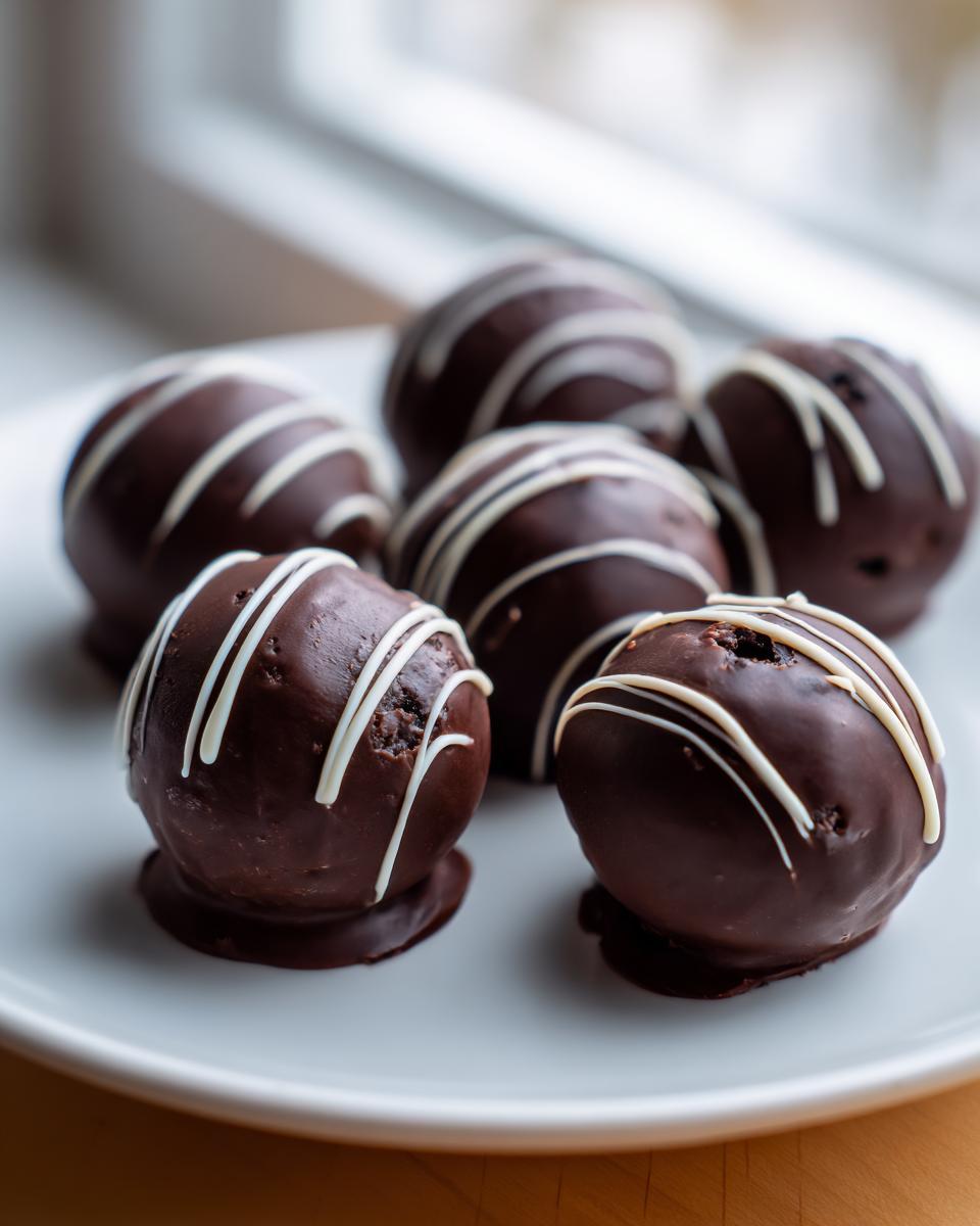 A close-up of several rich, dark chocolate covered oreo balls drizzled with white chocolate on a white plate.