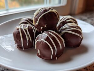 A small pile of rich, chocolate-covered oreo balls drizzled with white chocolate on a white plate.