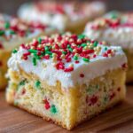 A close-up of a single serving of christmas sugar cookie bars topped with thick white frosting and red, green, and gold sprinkles.