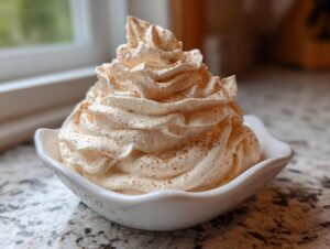 A swirl of light brown, fluffy cinnamon butter topping dusted with spice, served in a small white dish.