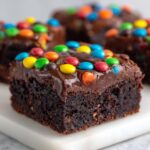 A close-up of a fudgy square cosmic brownie topped with chocolate frosting and colorful candy-coated chocolates.