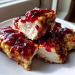 Close-up of cut pieces of cranberry chicken showing moist white meat topped with bright red cranberry sauce.