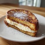 A thick slice of golden brown cream cheese stuffed french toast dusted with powdered sugar.
