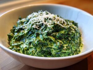 A close-up of rich, vibrant green creamed spinach recipe topped with freshly grated Parmesan cheese in a white bowl.