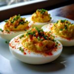 Four creamy deviled eggs topped with bright yellow filling, paprika, and fresh green chives on a white plate.