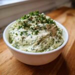 A close-up of a fluffy bowl of homemade dill dip, generously topped with fresh herbs.