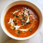 Close-up of creamy tomato basil soup garnished with a swirl of cream and fresh basil leaves.