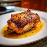 Close-up of a single, perfectly cooked braised chicken thighs piece with crispy, browned skin resting in its savory pan sauce.
